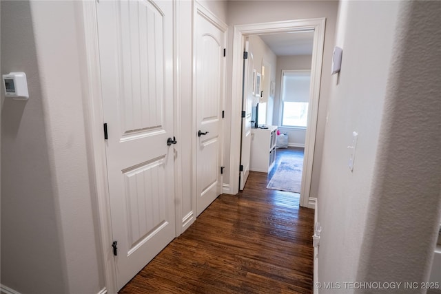 corridor featuring dark wood-type flooring and baseboards