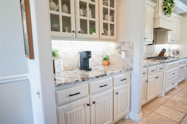 bar area with stainless steel gas cooktop, decorative backsplash, custom exhaust hood, and stone tile floors