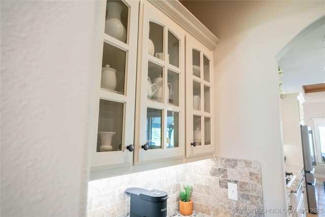 kitchen view of arched walkways, stucco siding, freestanding refrigerator, and glass insert cabinets