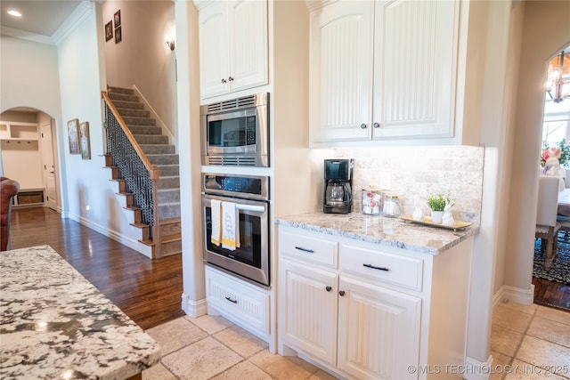 kitchen with appliances with stainless steel finishes, arched walkways, light stone counters, baseboards, and tasteful backsplash