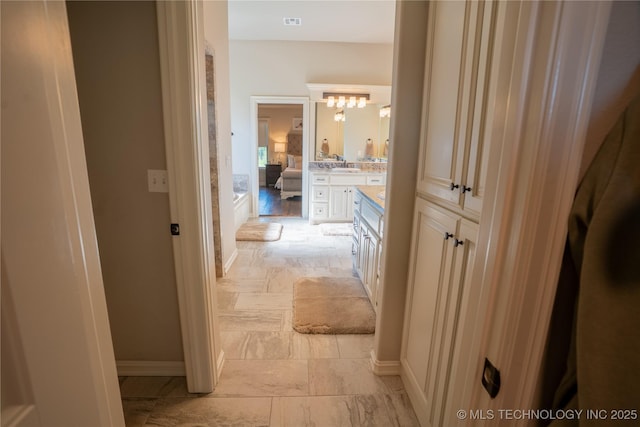 corridor with baseboards, a sink, and a chandelier