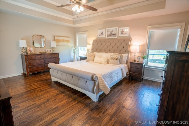 bedroom with a tray ceiling, ornamental molding, dark wood-type flooring, a ceiling fan, and baseboards