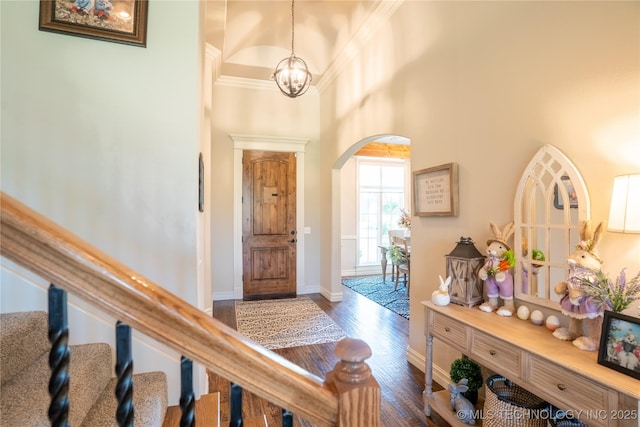 entryway with arched walkways, dark wood finished floors, a towering ceiling, a chandelier, and baseboards
