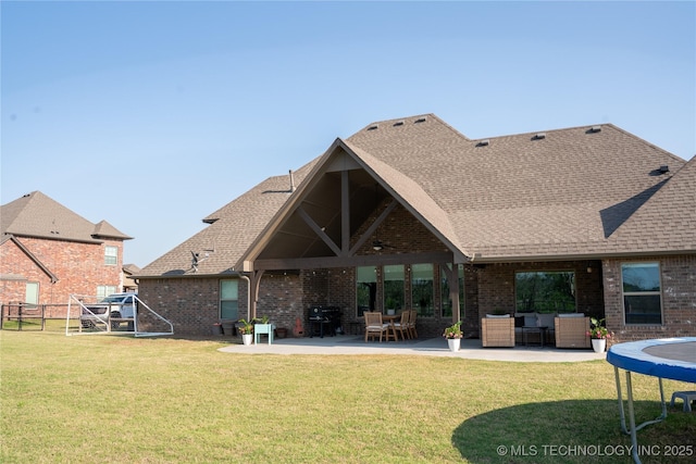 rear view of property with brick siding, a patio area, a trampoline, and roof with shingles