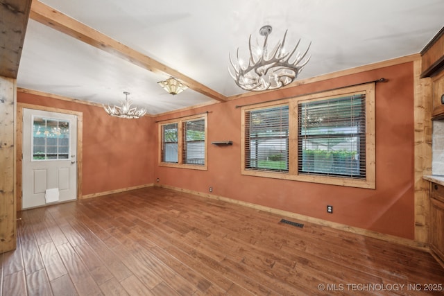 unfurnished dining area with a chandelier, wood finished floors, baseboards, and beamed ceiling