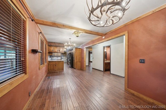 unfurnished living room featuring a chandelier, beamed ceiling, dark wood-style floors, baseboards, and healthy amount of natural light