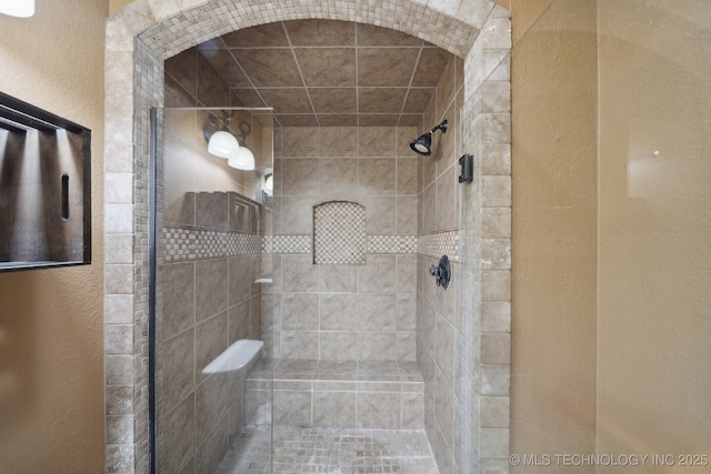 bathroom featuring tiled shower and a textured wall