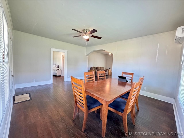 dining area with wood finished floors, arched walkways, a ceiling fan, baseboards, and ornamental molding