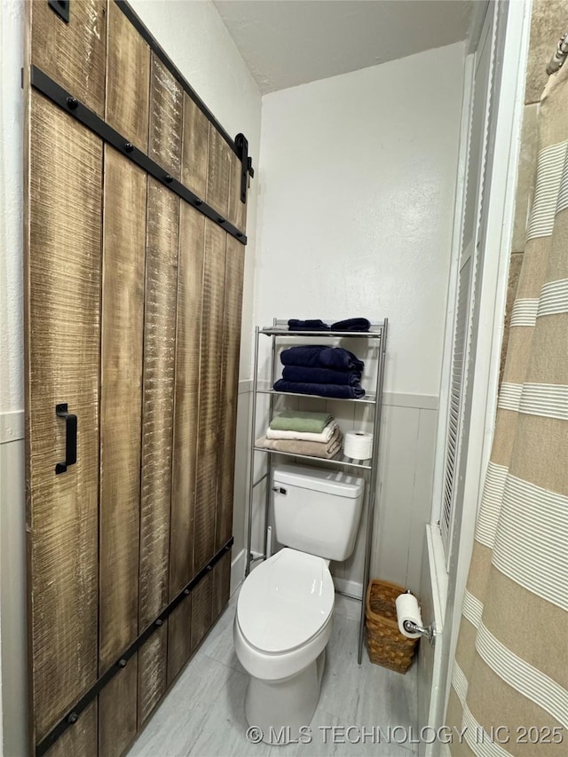 bathroom featuring toilet and a wainscoted wall