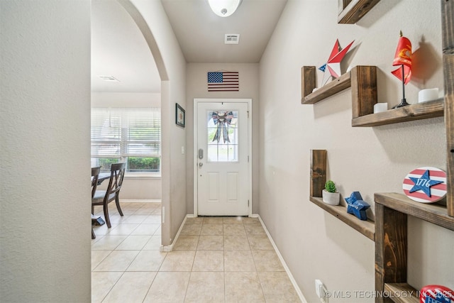 entryway featuring arched walkways, light tile patterned floors, and baseboards
