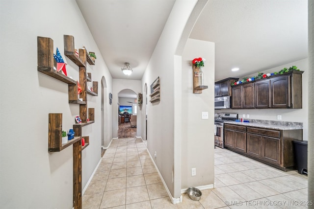 hall featuring arched walkways, light tile patterned floors, and baseboards