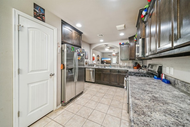 kitchen featuring appliances with stainless steel finishes, dark brown cabinets, light tile patterned floors, arched walkways, and recessed lighting