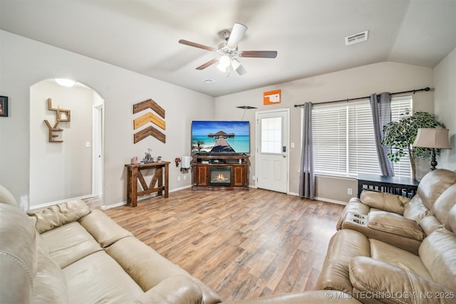 living area featuring light wood-style floors, ceiling fan, baseboards, arched walkways, and lofted ceiling