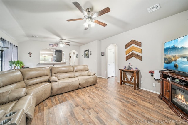 living room with arched walkways, light wood-type flooring, ceiling fan, baseboards, and vaulted ceiling