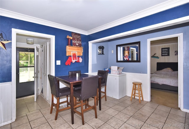 dining area with light tile patterned flooring, a wainscoted wall, and crown molding