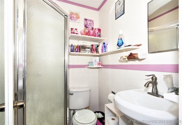 bathroom with a sink, tile walls, toilet, a stall shower, and ornamental molding