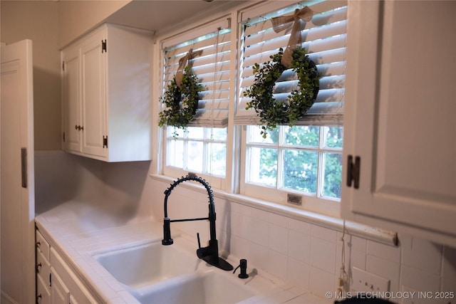 kitchen featuring a sink, tile countertops, and white cabinets
