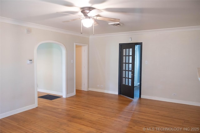 spare room with arched walkways, a ceiling fan, light wood-style floors, crown molding, and baseboards