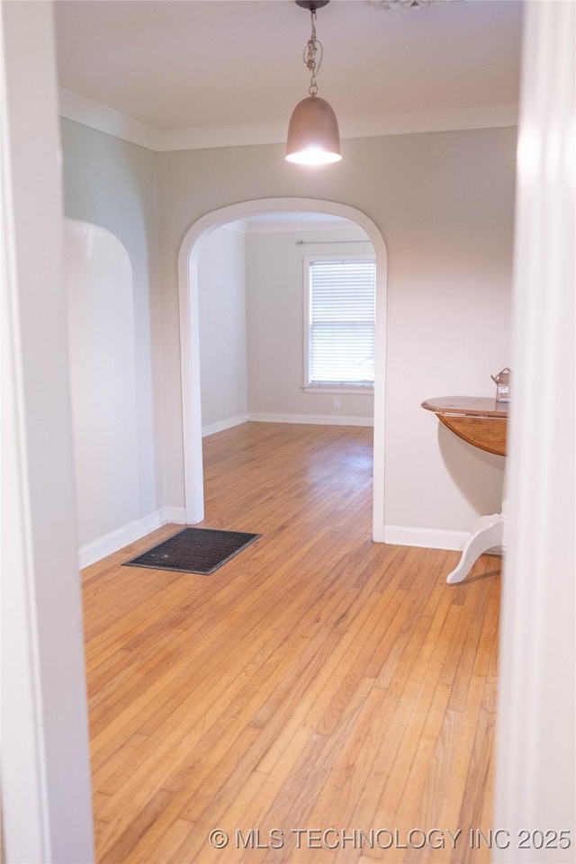 corridor featuring arched walkways, hardwood / wood-style floors, crown molding, and baseboards