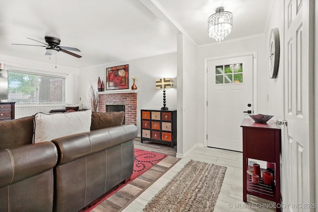 foyer featuring ceiling fan, ornamental molding, a chandelier, a brick fireplace, and baseboards