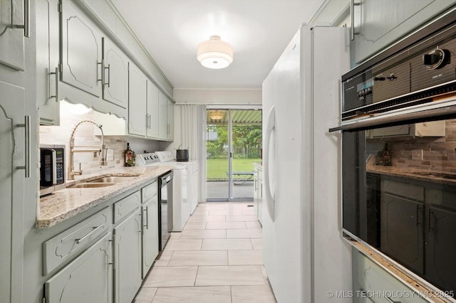 kitchen featuring a sink, washing machine and dryer, appliances with stainless steel finishes, decorative backsplash, and light stone counters