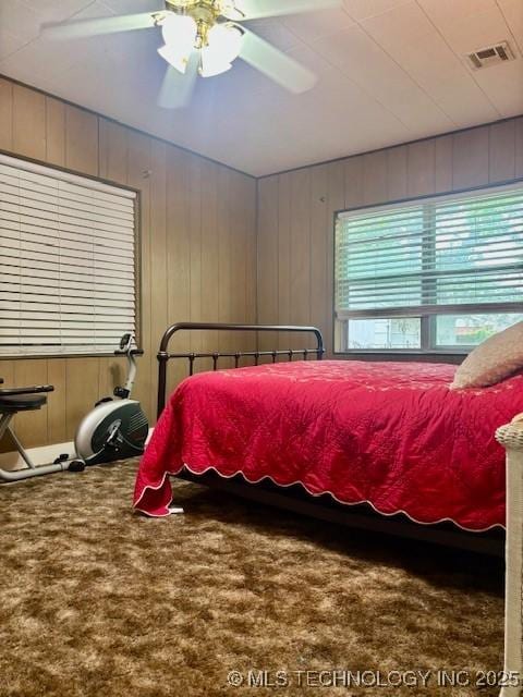 carpeted bedroom featuring ceiling fan and wooden walls