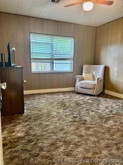 sitting room with a ceiling fan, healthy amount of natural light, carpet flooring, baseboards, and wooden walls