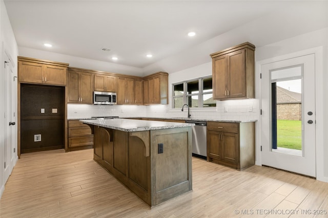 kitchen with stainless steel appliances, a center island, brown cabinets, a sink, and backsplash