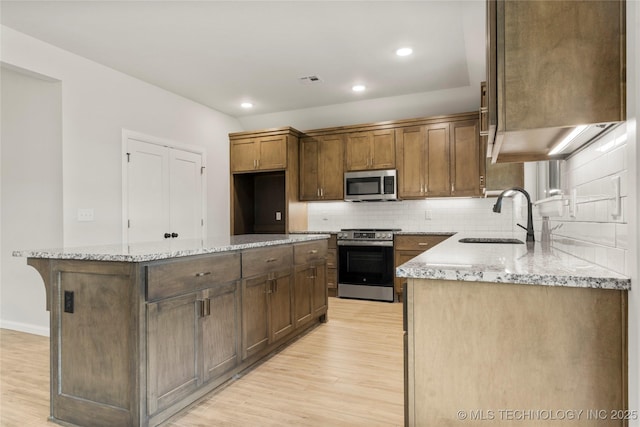 kitchen featuring appliances with stainless steel finishes, a sink, light wood-style flooring, backsplash, and a kitchen island