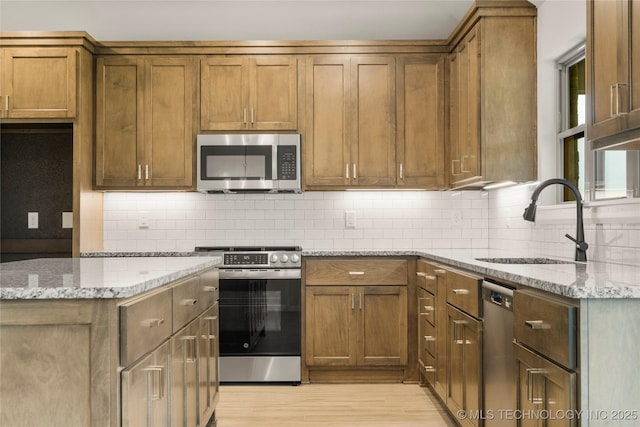 kitchen featuring stainless steel appliances, a sink, light stone counters, light wood-style floors, and brown cabinetry