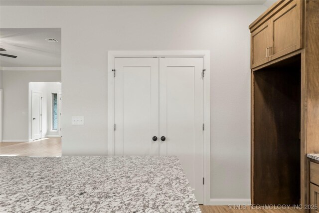 kitchen featuring light wood-style flooring, baseboards, ceiling fan, brown cabinetry, and light stone counters