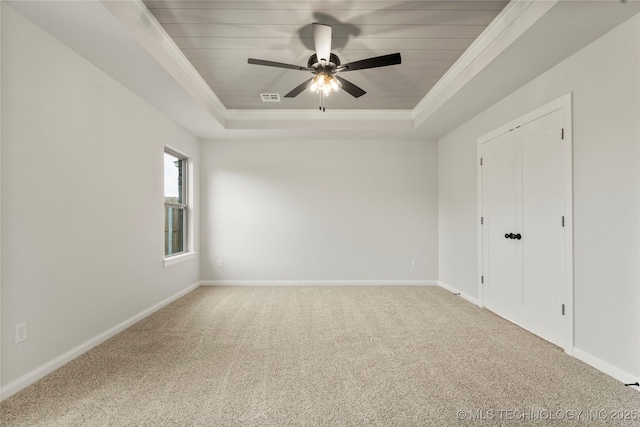 carpeted spare room with a raised ceiling, baseboards, ornamental molding, and a ceiling fan