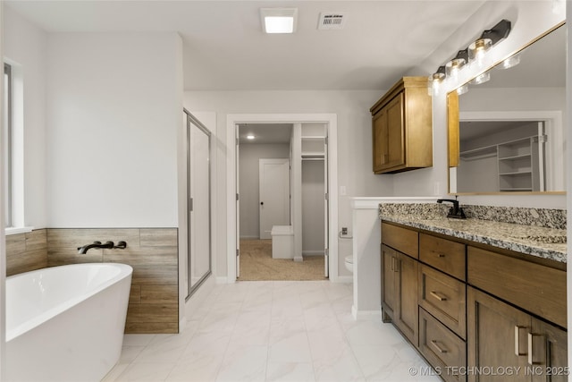 bathroom featuring a shower stall, marble look tile flooring, vanity, a freestanding tub, and a spacious closet