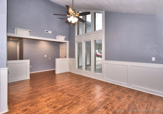 unfurnished living room with ceiling fan, high vaulted ceiling, wood finished floors, a decorative wall, and a wainscoted wall