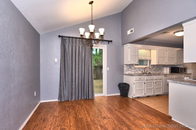 kitchen with stainless steel microwave, dishwasher, a sink, white cabinetry, and vaulted ceiling