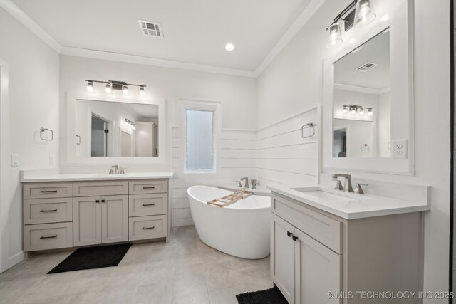 bathroom featuring a freestanding bath, two vanities, crown molding, and tile patterned flooring