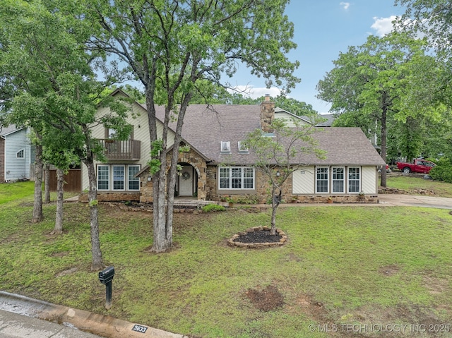 view of front facade featuring a front yard, stone siding, a shingled roof, and a chimney