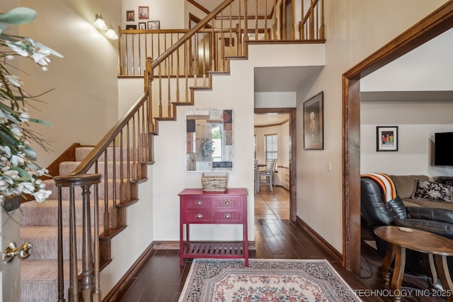 foyer featuring stairs, wood finished floors, a towering ceiling, and baseboards