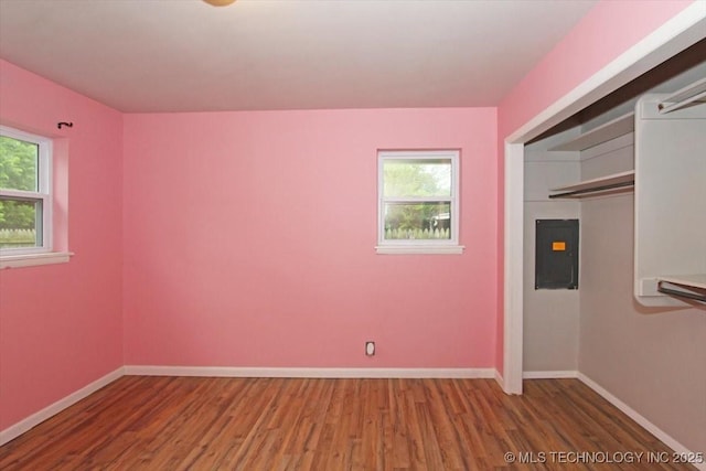 unfurnished bedroom featuring wood finished floors, multiple windows, baseboards, and electric panel