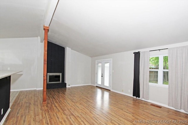 unfurnished living room featuring lofted ceiling, light wood-type flooring, and a brick fireplace