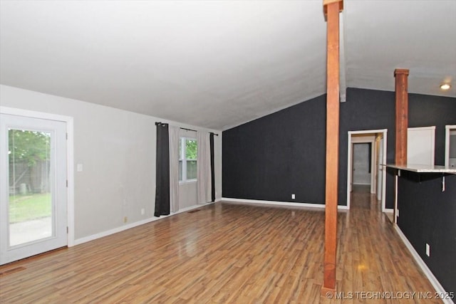 unfurnished living room featuring vaulted ceiling, wood finished floors, plenty of natural light, decorative columns, and baseboards