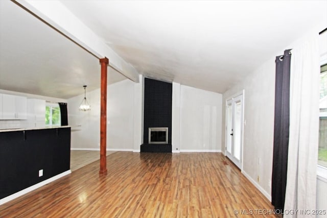 unfurnished living room with light wood-type flooring, a brick fireplace, a chandelier, and baseboards