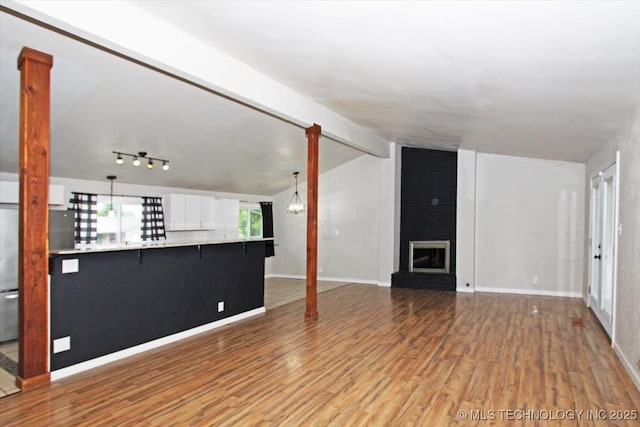 unfurnished living room with light wood finished floors, a brick fireplace, and baseboards