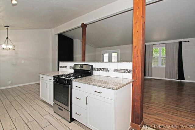 kitchen featuring stainless steel gas stove, light wood-type flooring, light stone countertops, white cabinetry, and vaulted ceiling