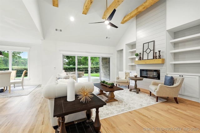 living area with high vaulted ceiling, ceiling fan, light wood-style flooring, plenty of natural light, and a fireplace