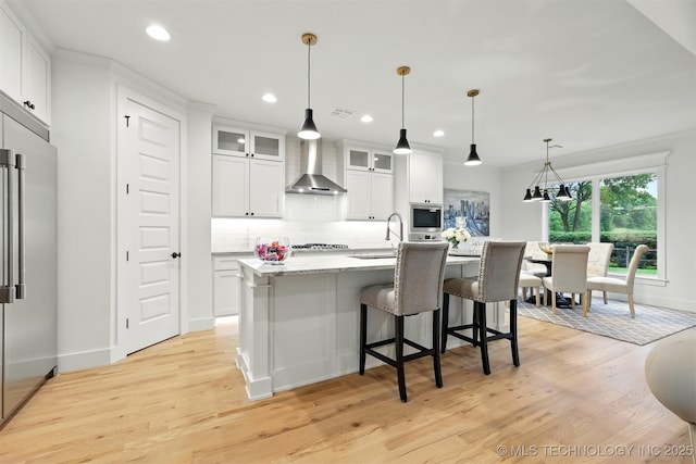 kitchen featuring wall chimney exhaust hood, stainless steel appliances, a sink, light wood-style floors, and backsplash