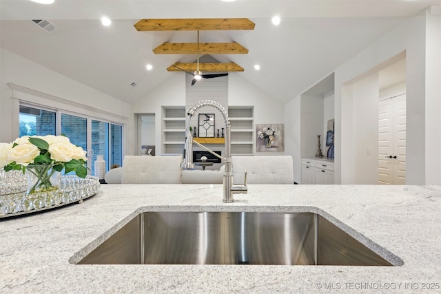 kitchen with a sink, light stone counters, open floor plan, built in features, and recessed lighting