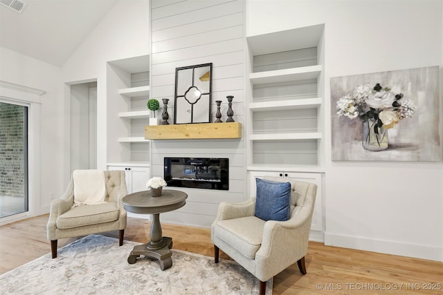 living area with wood finished floors, built in features, a glass covered fireplace, baseboards, and high vaulted ceiling