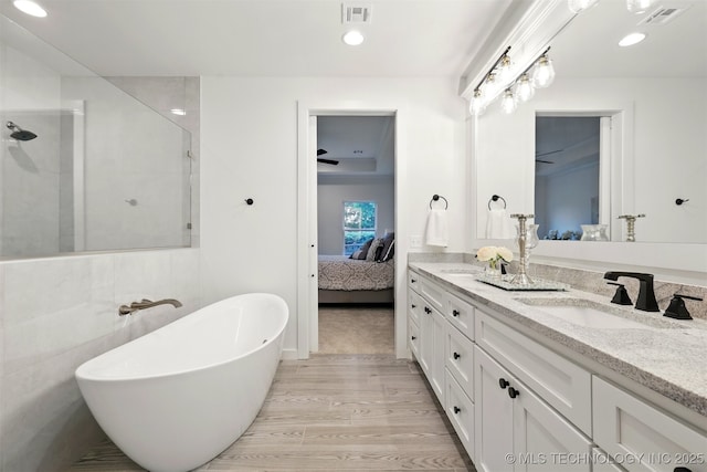 ensuite bathroom featuring a tile shower, wood finished floors, double vanity, a freestanding tub, and recessed lighting