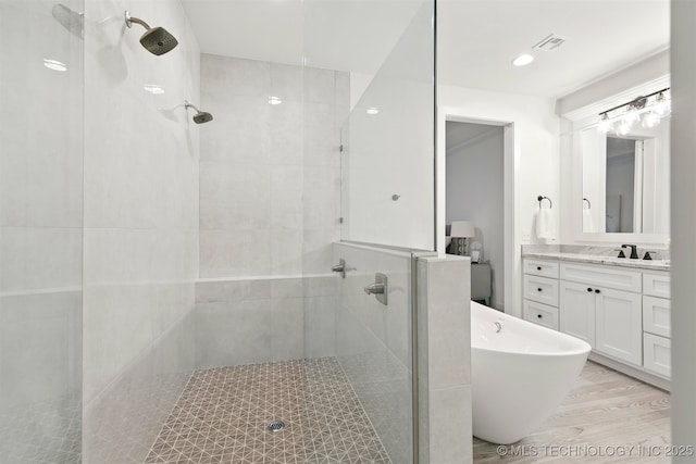bathroom featuring a tile shower, vanity, wood finished floors, and a soaking tub